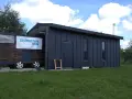 Mobilny garaż bez pozwolenia, z banerem "Zbuduj sam dom", stoi na trawie.