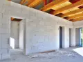 Wnętrze domu w budowie, ściany z bloczków suporeks, widoczne drewniane belki stropowe.