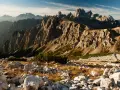 Skaliste szczyty Dolomitów o wschodzie słońca, z kamienistym zboczem i suchą trawą na pierwszym planie.