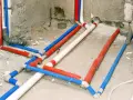 Skomplikowana instalacja wodna z rurami w kolorach czerwonym, niebieskim i białym, przygotowana do tynkowania.