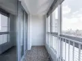 Nowoczesna zabudowa balkonu w bloku z widokiem na miasto. Szklane drzwi i okna tworzą przestronne wnętrze.