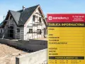 Tablica informacyjna budowy domu w trakcie prac. Widoczny dom w rusztowaniach i żółta tablica z danymi budowy.
