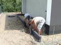 Dwóch mężczyzn układa obrzeża. Prawidłowe suchy beton proporcje są kluczowe dla trwałości.