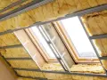 Ocieplenie dachu z wełny mineralnej w trakcie montażu. Widoczne profile metalowe i okna dachowe.