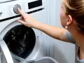 Kobieta naciska przycisk na pralce, która nie pobiera wody. Zastanawia się, dlaczego pranie nie rusza.