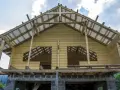 Drewniana wiata przy domu w budowie, z widoczną konstrukcją dachu i ścian z bali.