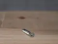 Metalowy konfirmat z gniazdem sześciokątnym leży na drewnianej powierzchni.