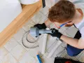 Hydraulik z narzędziem wuko naprawia odpływ pod umywalką.
