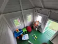 Jak urządzić domek dla dzieci w środku? Zabawki, stolik, kuchnia i pufy tworzą przytulną przestrzeń do zabawy.