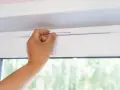 Dłoń reguluje biały nawiewnik okienny, zapewniając świeże powietrze w pomieszczeniu.