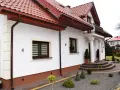 Biały dom z brązowymi cokołami, czerwonym dachem i ozdobnymi schodami.