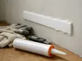 Klej Mamut schnie, a listwa przypodłogowa czeka na montaż. Rękawice i nożyk gotowe do pracy.