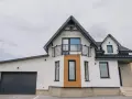 Nowoczesny dom z garażem i balkonem. Elegancki gzyms podkreśla architekturę budynku, a drewniane elementy dodają ciepła.