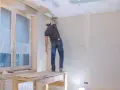 Pracownik szpachluje łączenia płyt gipsowych na suficie. Poznaj szpachlowanie łączeń płyt gipsowych cena.