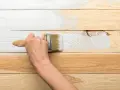 Ręka maluje białą farbą drewnianą boazerię, odnawiając jej wygląd.