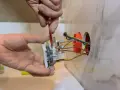 Instalator pokazuje, jak podłączyć gniazdko, przykręcając je do ściany. Widać przewody elektryczne.