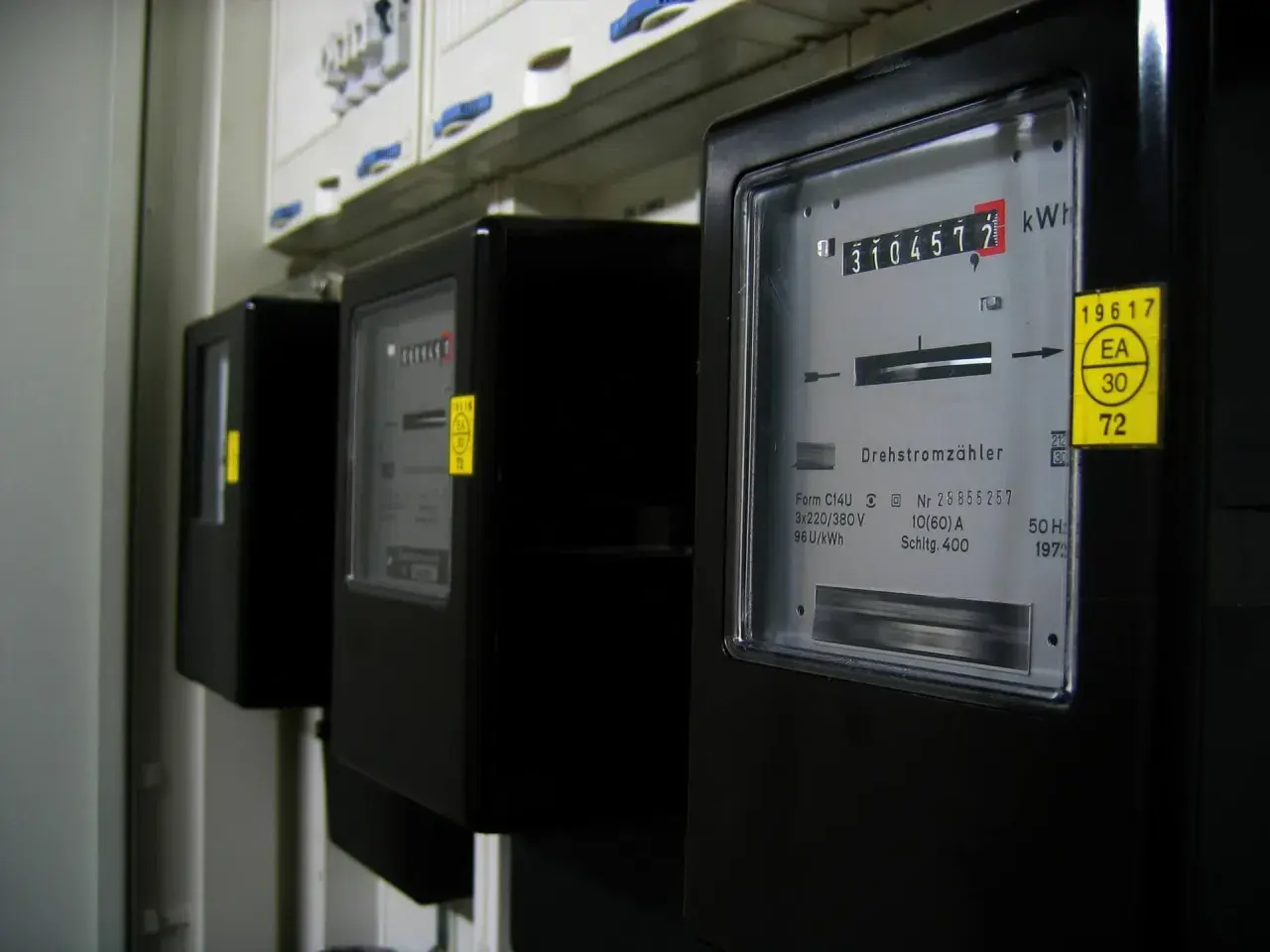 Rząd czarnych liczników energii elektrycznej. Na pierwszym liczniku widoczny odczyt 3104577 kWh.
