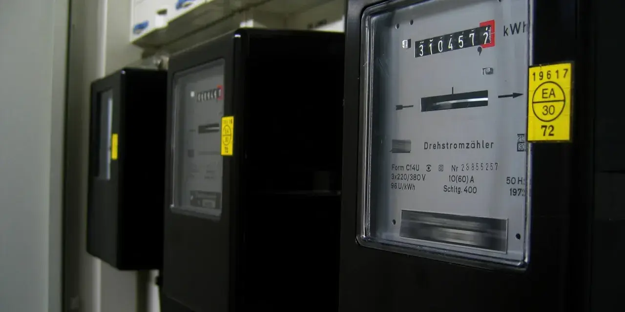 Rząd czarnych liczników energii elektrycznej. Na pierwszym liczniku widoczny odczyt 3104577 kWh.