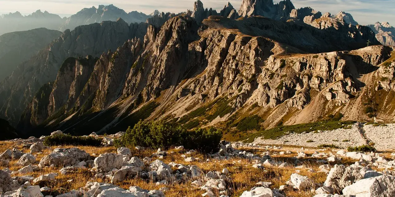 Skaliste szczyty Dolomitów o wschodzie słońca, z kamienistym zboczem i suchą trawą na pierwszym planie.