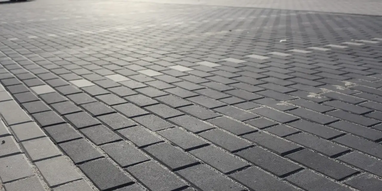 Szary parking wyłożony kostką brukową holland. W tle widać zaparkowane samochody.