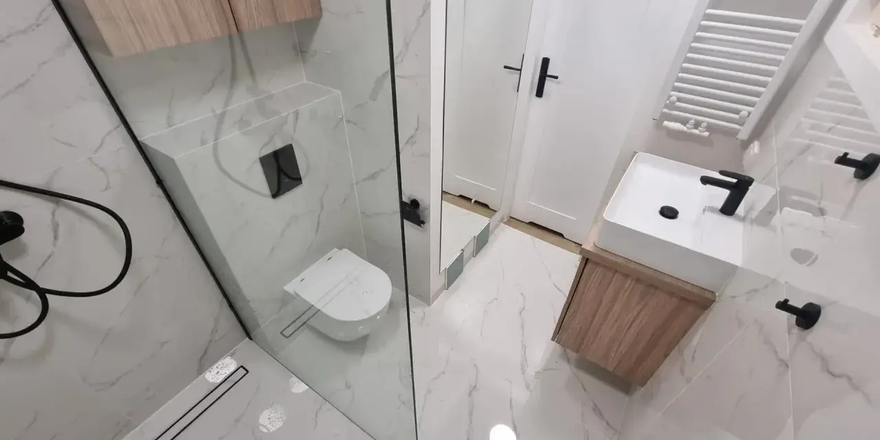 Nowoczesna łazienka z prysznicem walk-in, umywalką nablatową i podwieszaną toaletą. Eleganckie płytki imitujące marmur i drewniane akcenty. Remont łazienki koszt może być różny, ale efekt jest wart inwestycji.