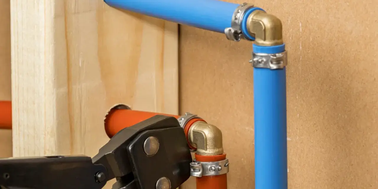 Instalacja hydrauliczna z rurami pex. Narzędzie do zaciskania łączy pomarańczową rurę z mosiężnym kolankiem.