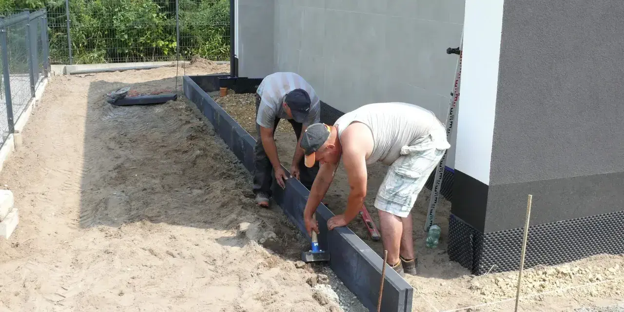 Dwóch mężczyzn układa obrzeża. Prawidłowe suchy beton proporcje są kluczowe dla trwałości.