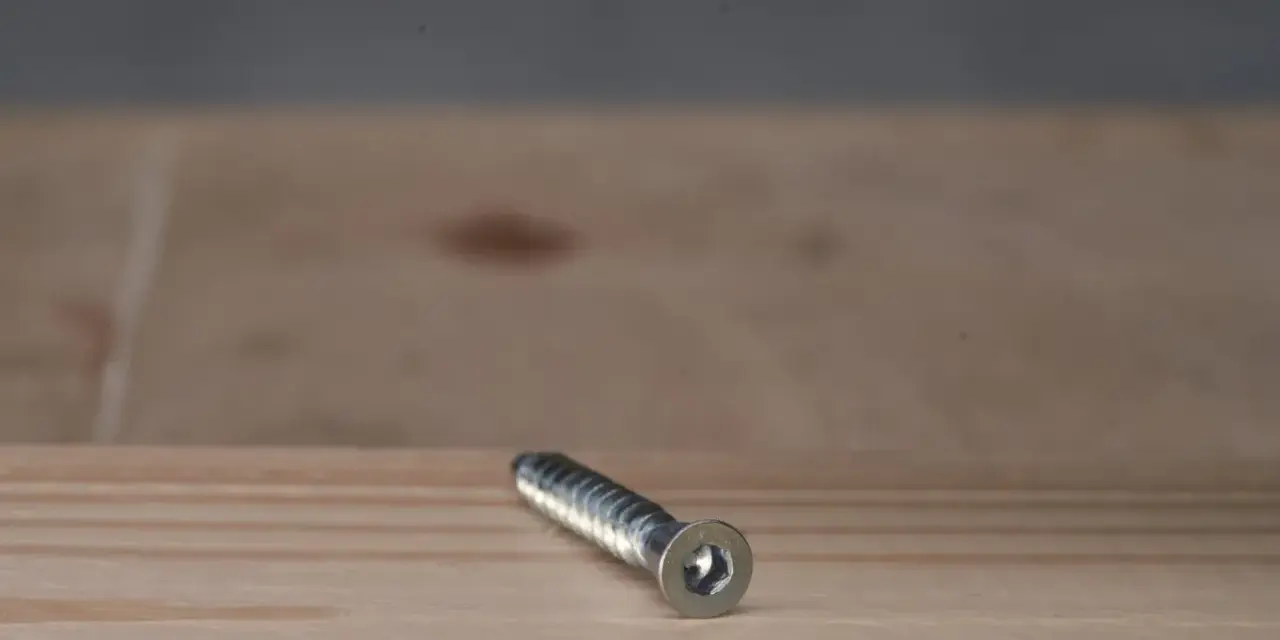 Metalowy konfirmat z gniazdem sześciokątnym leży na drewnianej powierzchni.
