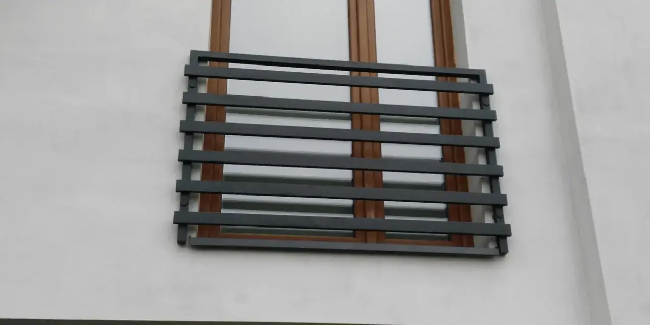 Nowoczesne balkony francuskie z ciemnoszarymi, poziomymi barierkami na tle białej ściany i brązowych okien.