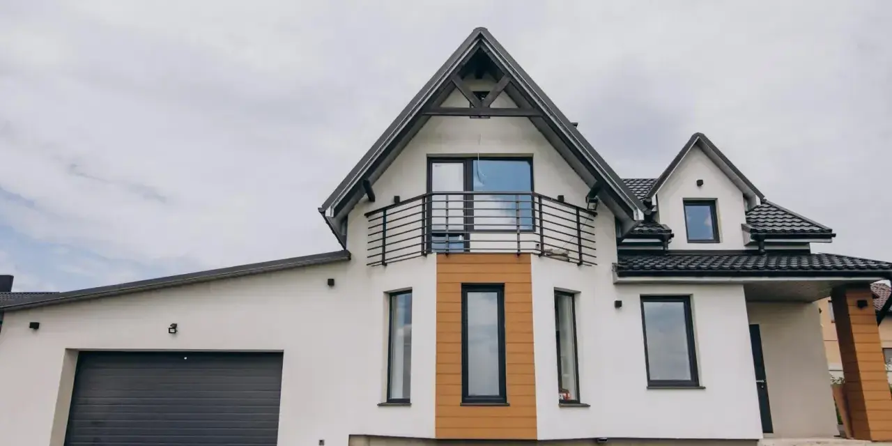 Nowoczesny dom z garażem i balkonem. Elegancki gzyms podkreśla architekturę budynku, a drewniane elementy dodają ciepła.