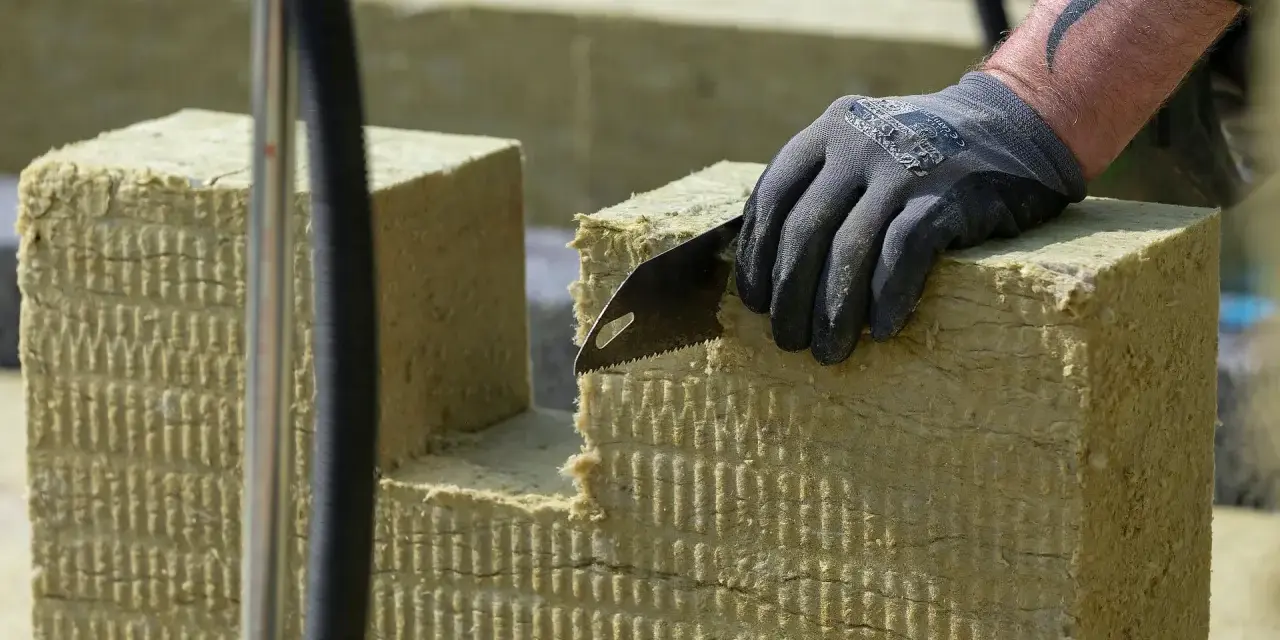 Ręka w rękawicy tnie piłą wełnę skalną 10. Materiał izolacyjny jest cięty na budowie.