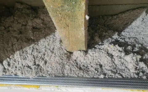 Luźna celuloza ocieplenie w przestrzeni między belkami stropowymi, widoczny metalowy profil.