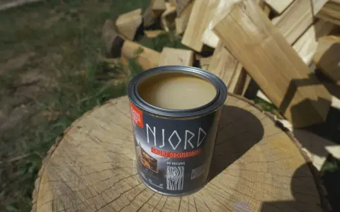 Otwarta puszka gruntu odcinającego NJORD na pniu drewna, w tle stos drewna opałowego.