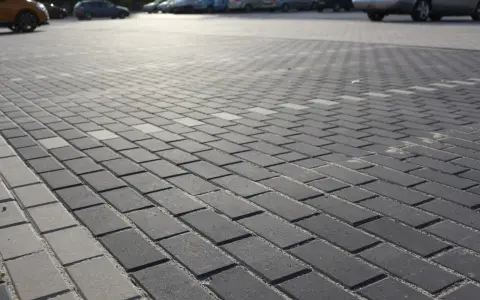 Szary parking wyłożony kostką brukową holland. W tle widać zaparkowane samochody.