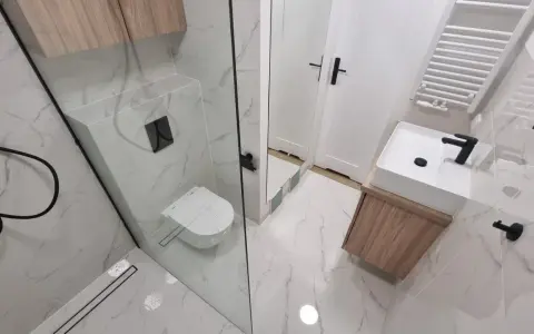 Nowoczesna łazienka z prysznicem walk-in, umywalką nablatową i podwieszaną toaletą. Eleganckie płytki imitujące marmur i drewniane akcenty. Remont łazienki koszt może być różny, ale efekt jest wart inwestycji.