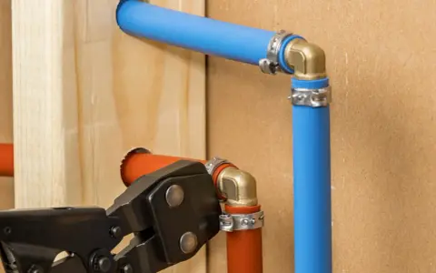 Instalacja hydrauliczna z rurami pex. Narzędzie do zaciskania łączy pomarańczową rurę z mosiężnym kolankiem.