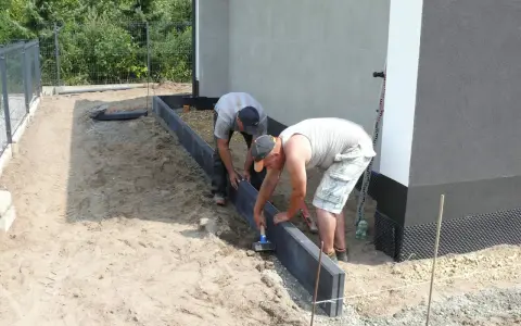 Dwóch mężczyzn układa obrzeża. Prawidłowe suchy beton proporcje są kluczowe dla trwałości.