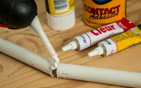 Aplikacja kleju butapren na pękniętą białą rurkę. W tle tubki z klejem i puszka "Contact Adhesive".