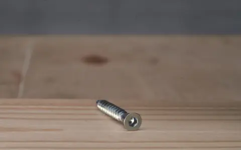 Metalowy konfirmat z gniazdem sześciokątnym leży na drewnianej powierzchni.