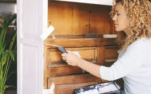 Kobieta odnawia mebel z forniru dębowego, malując go na biało wałkiem.