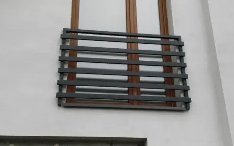 Nowoczesne balkony francuskie z ciemnoszarymi, poziomymi barierkami na tle białej ściany i brązowych okien.