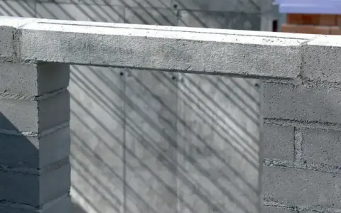 Szary betonowy nadproże opiera się na dwóch słupkach z bloczków. Cienie ukośnie przecinają tło.