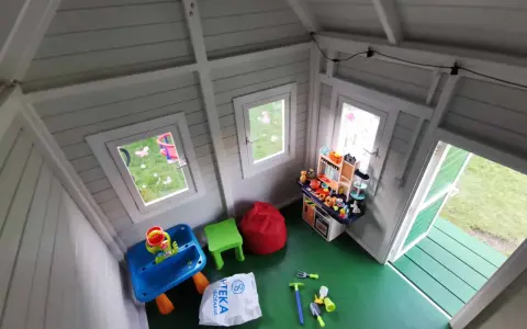 Jak urządzić domek dla dzieci w środku? Zabawki, stolik, kuchnia i pufy tworzą przytulną przestrzeń do zabawy.