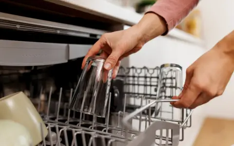 Ręce wkładają szklanki do zmywarki. To część poradnika, jak wybrać zmywarkę, pokazująca praktyczne użycie.