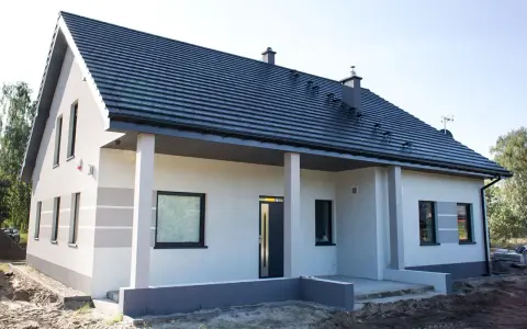 Nowy dom z szarą dachówką i jasną elewacją, gotowy do malowania. Eleganckie wykończenie podkreśla nowoczesny styl.