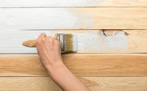 Ręka maluje białą farbą drewnianą boazerię, odnawiając jej wygląd.