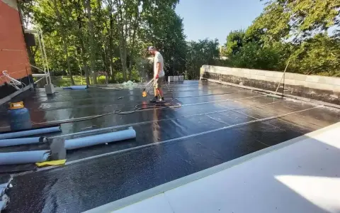 Pracownik wykonuje hydroizolację tarasu nad garażem, używając palnika do papy.