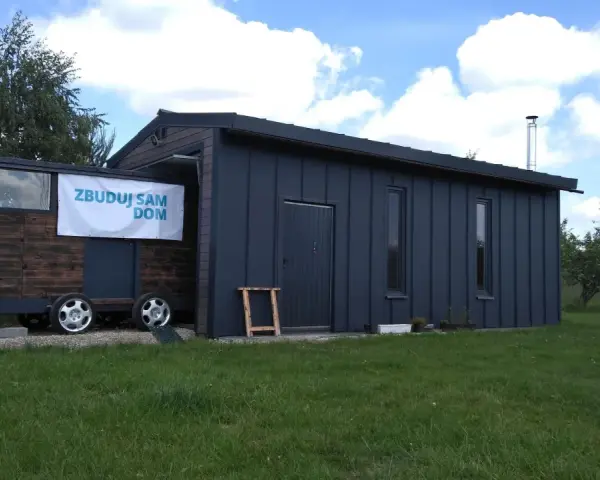 Mobilny garaż bez pozwolenia, z banerem "Zbuduj sam dom", stoi na trawie.