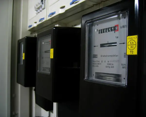 Rząd czarnych liczników energii elektrycznej. Na pierwszym liczniku widoczny odczyt 3104577 kWh.