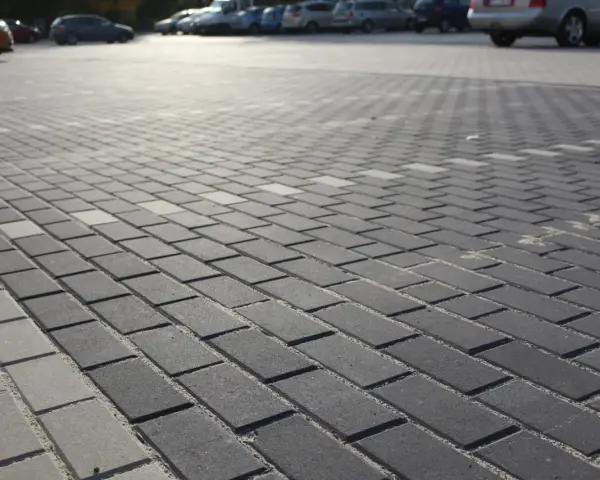 Szary parking wyłożony kostką brukową holland. W tle widać zaparkowane samochody.